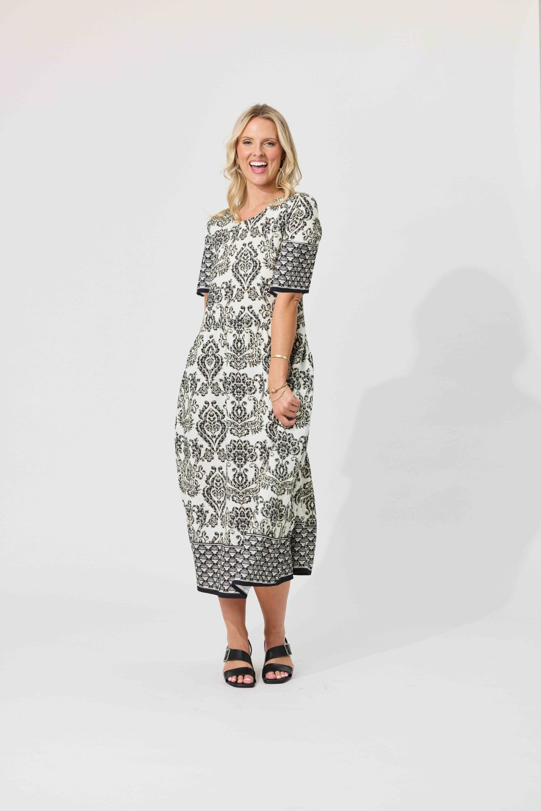 A woman modeling a short-sleeve midi dress with a black and white geometric pattern, standing against a plain white studio background.