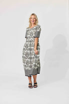 A woman modeling a short-sleeve midi dress with a black and white geometric pattern, standing against a plain white studio background.