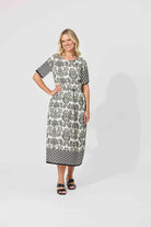 A woman modeling a short-sleeve midi dress with a black and white damask pattern, standing against a light gray studio background.