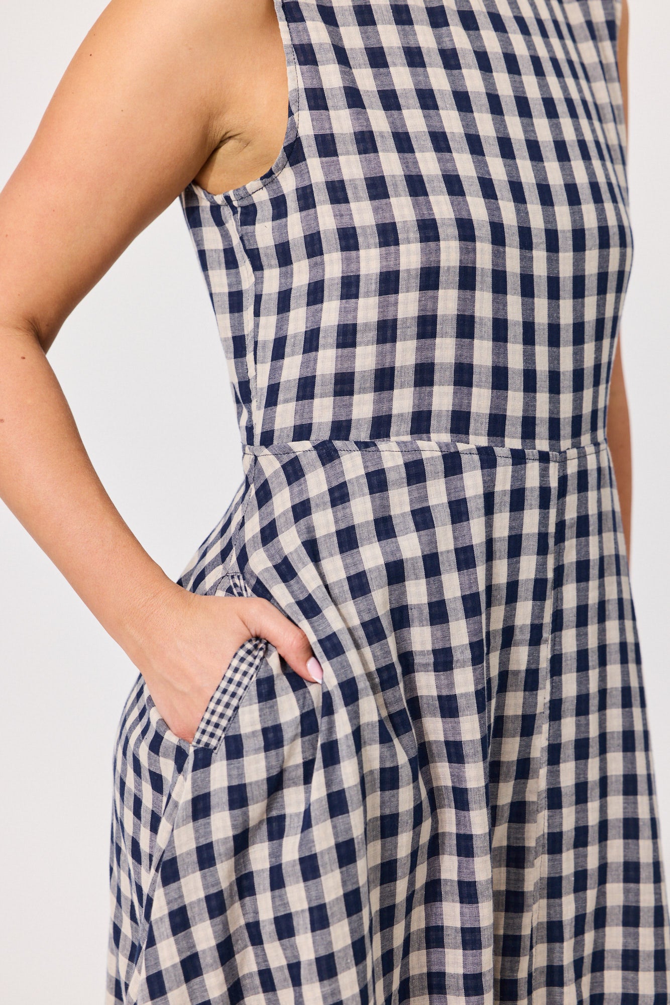 Close-up of a sleeveless navy and off-white gingham dress with a side pocket, shown on a model against a light gray background.