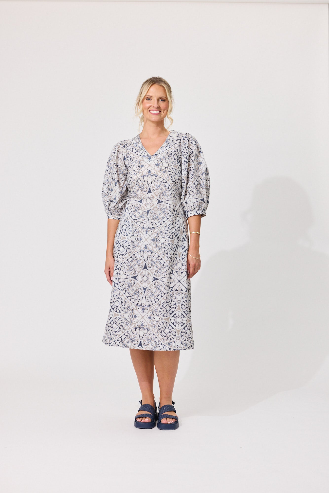 A woman modeling a knee-length puff-sleeve dress with a blue and white floral pattern, standing against a plain white studio background.