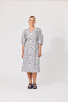 A woman modeling a knee-length puff-sleeve dress with a blue and white floral pattern, standing against a plain white studio background.