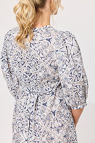 A woman shown from the back wearing a long-sleeve wrap-style dress with a blue, beige, and white paisley pattern and a tied waist belt.