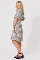 A woman modeling a short-sleeve knee-length dress with an intricate multicolor patchwork print, shown from a side-back angle against a plain white studio background.