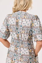 A woman shown from the back wearing a short-sleeve dress with a detailed geometric and tribal-inspired print in blue, yellow, brown, and black on a cream background.