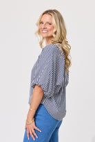 A woman with blonde hair is shown from a side-back angle wearing a navy and white vertically striped bubble-sleeve top and blue jeans against a plain light gray background.