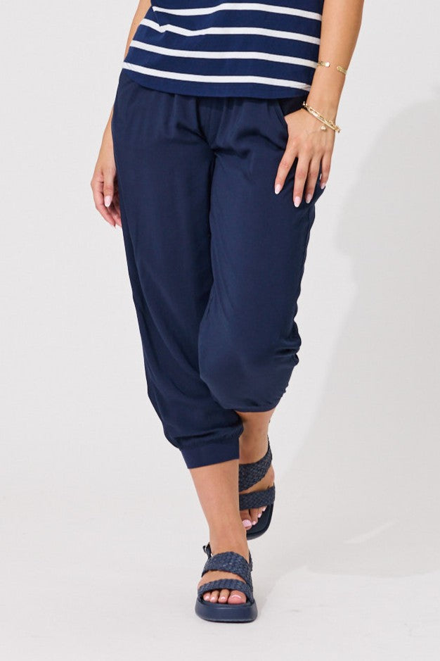 A person modeling navy blue cropped pants with a striped navy and white top and navy sandals, shown from the waist down against a plain light background.