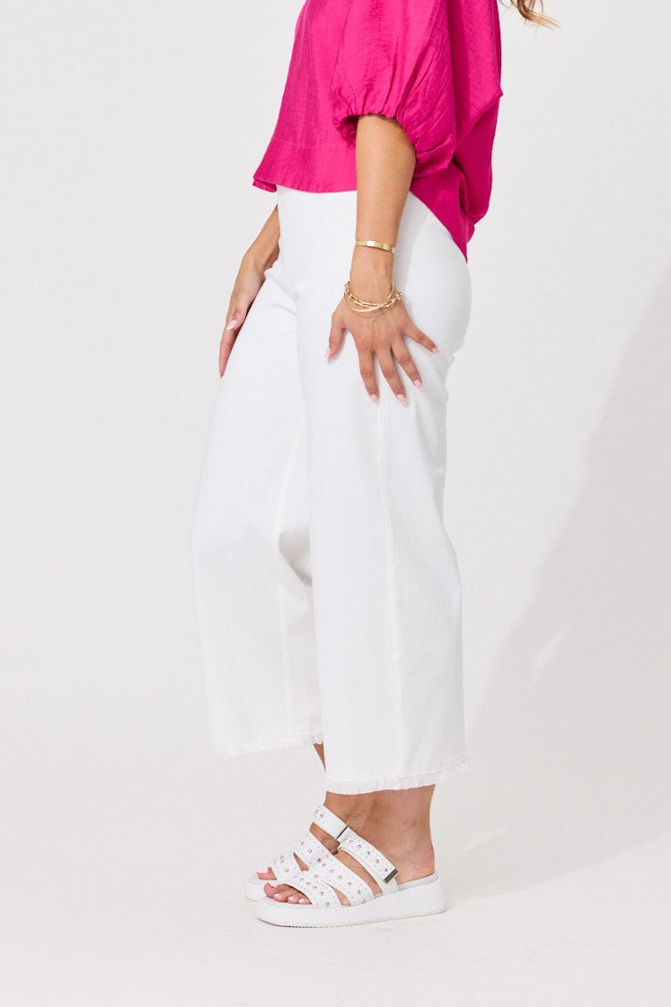A model wearing white wide-leg cropped pants, a bright pink puff-sleeve top, and white strappy sandals, shown from the waist down against a plain white studio background.