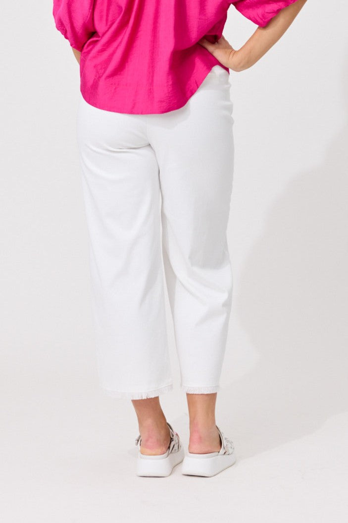 White cropped pants worn by a model, paired with a bright pink top and white platform sneakers, shown from the back against a plain white studio background.