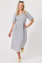 A woman modeling a short-sleeve midi dress with a small black and white gingham pattern, standing against a plain white studio background.