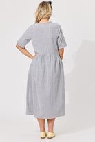 A woman viewed from the back wearing a short-sleeve midi dress with a small black and white gingham pattern, paired with pale yellow shoes against a plain light background.