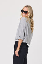 A woman wearing a black and white gingham cropped blouse with three-quarter sleeves and black pants, photographed against a plain light gray studio background.