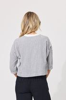 A woman viewed from behind wearing a cropped long-sleeve top with a small black and white gingham pattern, paired with dark pants, against a plain light gray background.