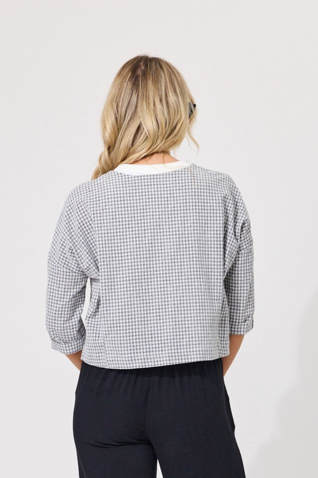 A woman viewed from behind wearing a cropped long-sleeve top with a small black and white gingham pattern, paired with dark pants, against a plain light gray background.