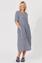 A woman modeling a short-sleeve midi dress with vertical navy and white stripes, standing against a plain white studio background.