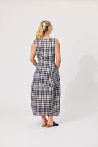 A woman viewed from behind wearing a sleeveless black and white gingham midi dress with pockets, paired with dark blue slip-on shoes, against a plain white studio background.