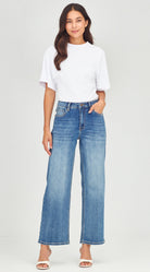 Woman wearing a white t-shirt and blue jeans on a plain background