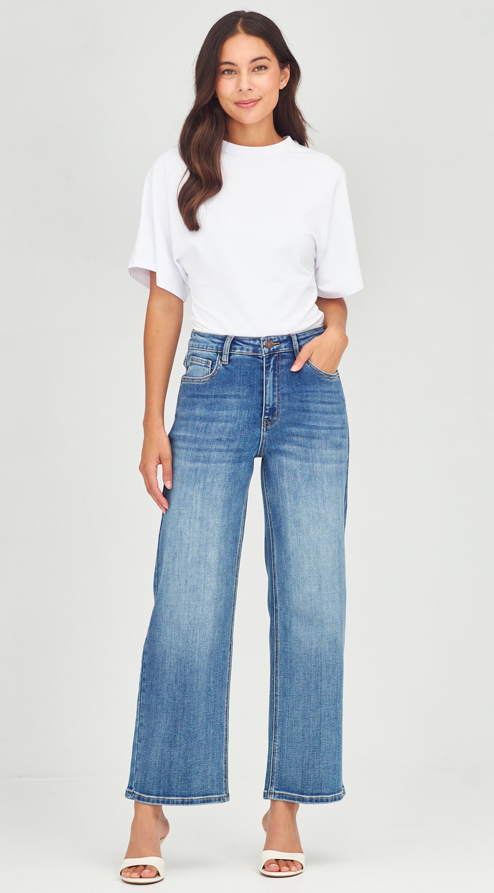 Woman wearing a white t-shirt and blue jeans on a plain background