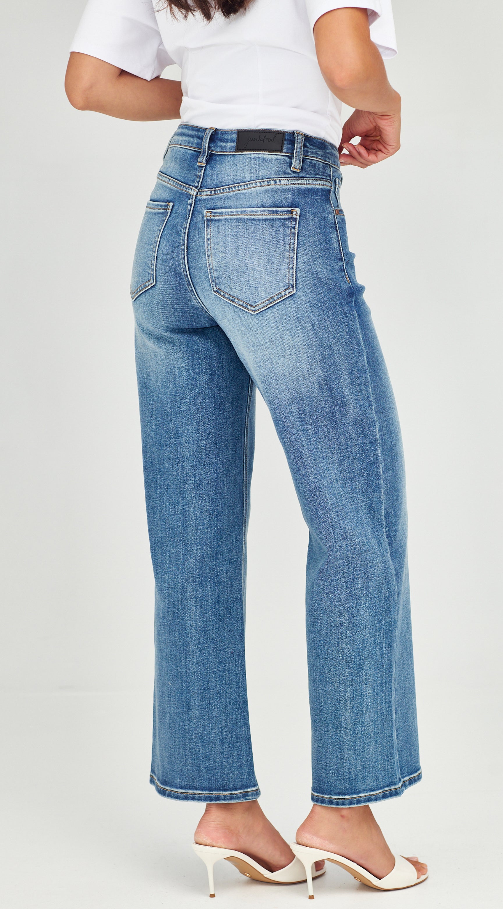 Person wearing blue jeans and a white top on a light gray background