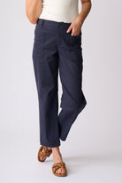 A person wearing dark navy cropped pants with a white top and brown woven slide sandals, standing against a light gray studio background.