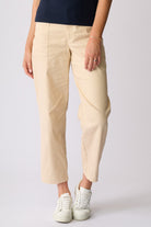 A person wearing light beige cropped trousers with a navy top and white sneakers, standing against a light gray studio background.