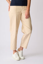 A person wearing light beige cropped trousers with a dark navy top and white sneakers, shown from the waist down against a plain light gray studio background.