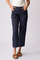 A person wearing navy cropped pants with a cream top and brown sandals, standing against a light gray studio background.