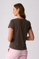 A woman shown from the back wearing a dark brown short-sleeve top and pink and white striped pants against a light gray studio background.