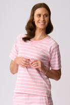 A woman wearing a light pink and white striped short-sleeve top, standing against a solid light gray studio background.