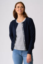 A woman modeling a navy blue cardigan with a black and white chevron pattern on the placket, worn over a black and white striped t-shirt and blue jeans, against a light gray studio background.
