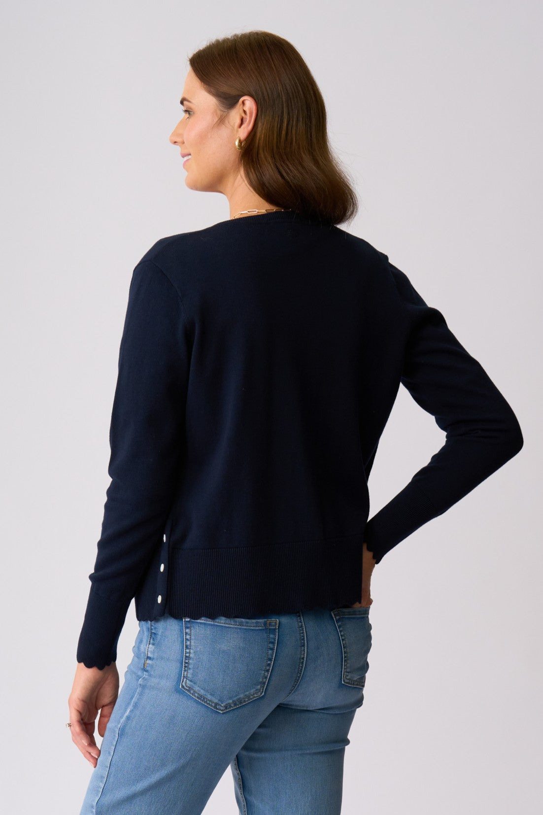 A woman shown from the back wearing a dark navy blue long-sleeve knit top and light blue jeans, standing against a light gray studio background.