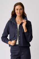 A woman modeling a navy blue cropped utility jacket with a high collar, snap buttons, and front flap pockets, paired with matching navy pants against a light gray studio background.