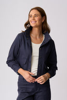 A woman modeling a navy blue lightweight utility jacket with snap-button details and flap pockets, worn over a white top and matching navy pants, against a light gray studio background.