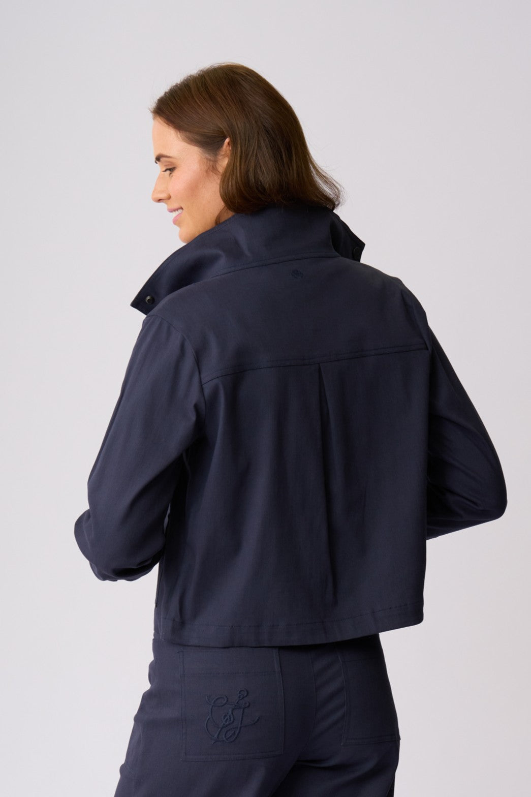 A woman shown from the back wearing a dark navy cropped jacket and matching navy trousers against a light gray studio background.