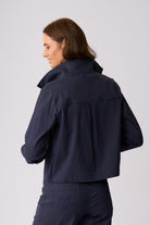 A woman shown from the back wearing a dark navy cropped jacket and matching navy trousers against a light gray studio background.