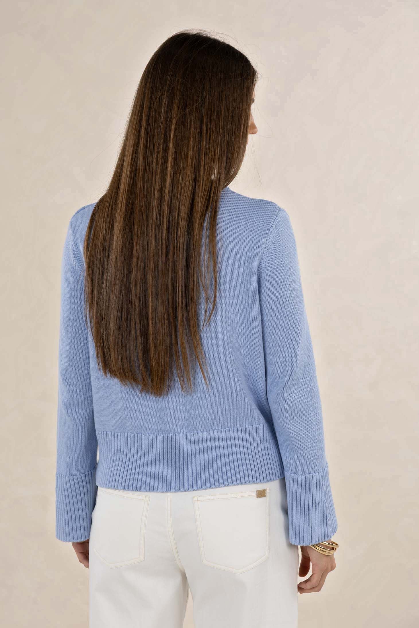 Woman wearing a light blue sweater and white pants against a beige background