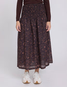 Person wearing a dark floral skirt with a plain background