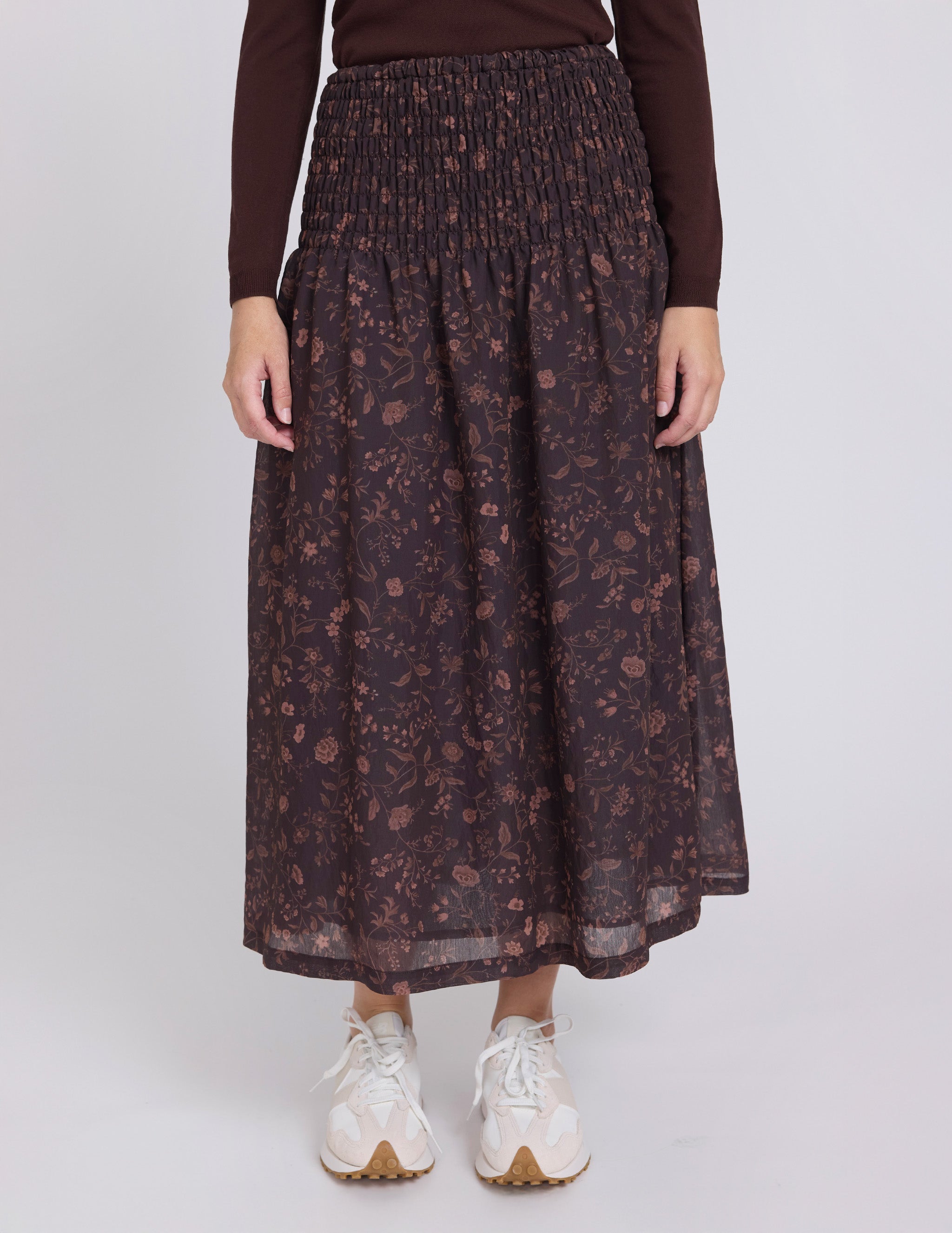 Person wearing a dark floral skirt with a plain background