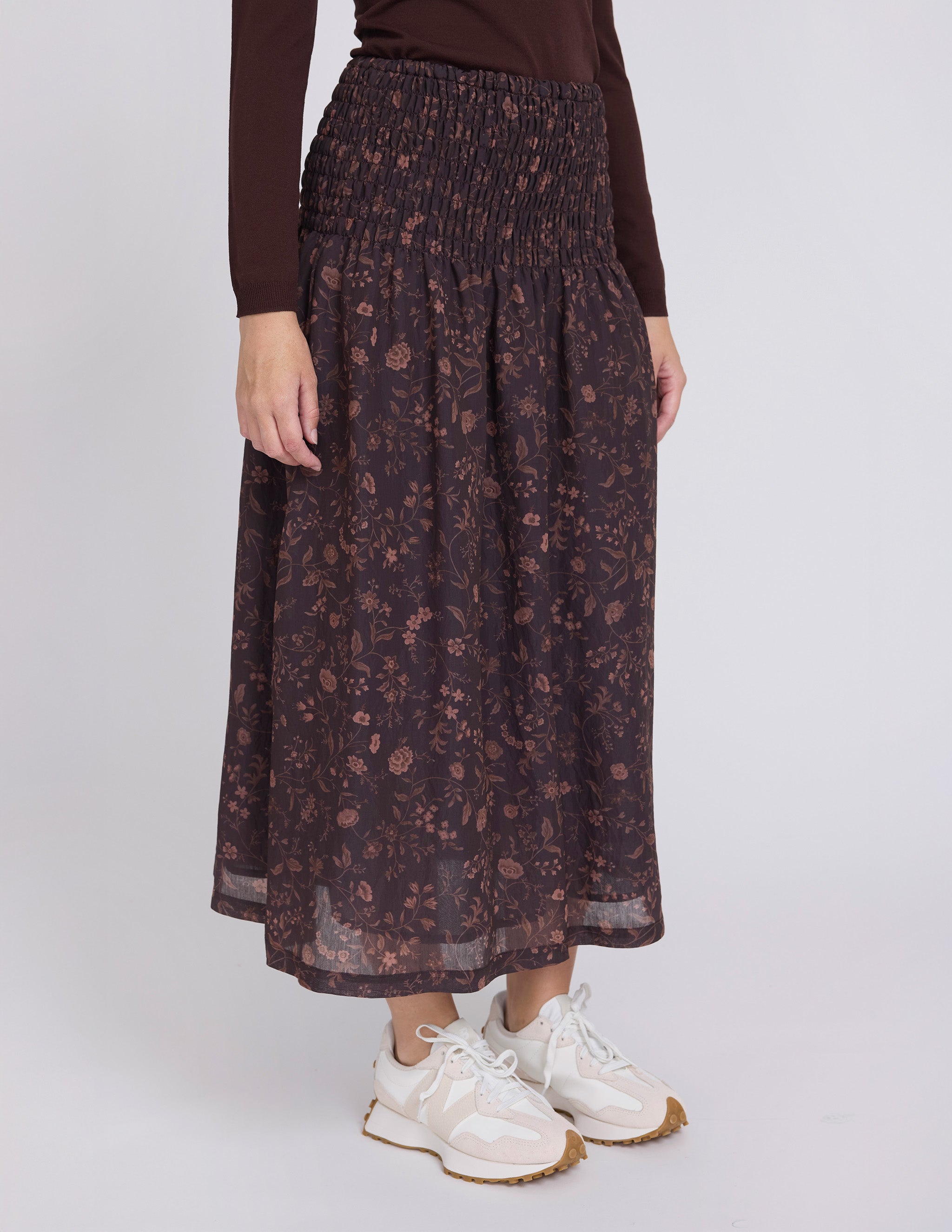Person wearing a dark floral skirt with white sneakers on a plain background