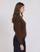 Woman wearing a brown sweater and dark jeans against a white background