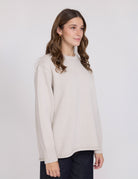 Woman wearing a beige sweater against a white background
