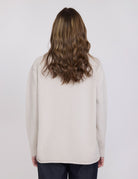 Person wearing a beige sweater with long hair on a white background