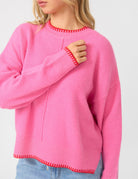 Person wearing a pink sweater with red trim on a light gray background