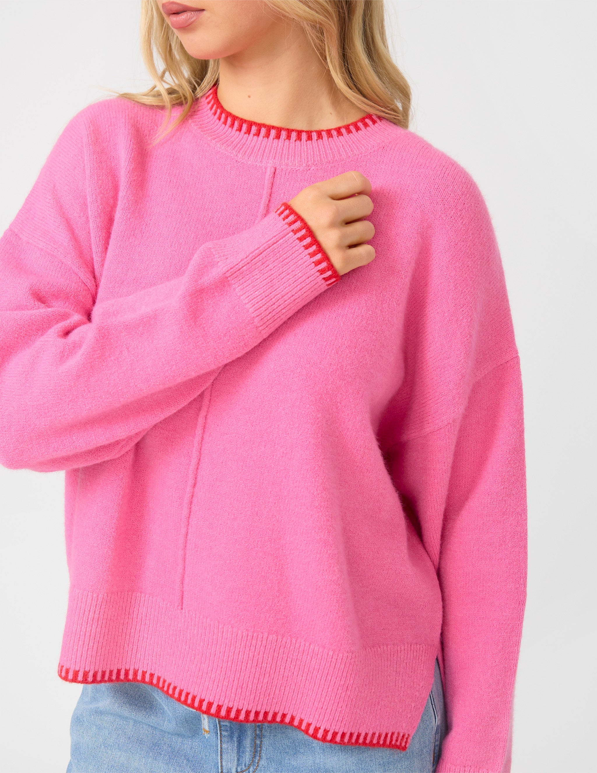 Person wearing a pink sweater with red trim on a light gray background