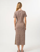 A woman viewed from the back wearing a short-sleeve leopard-print midi dress with a side slit, standing against a plain light gray studio background.