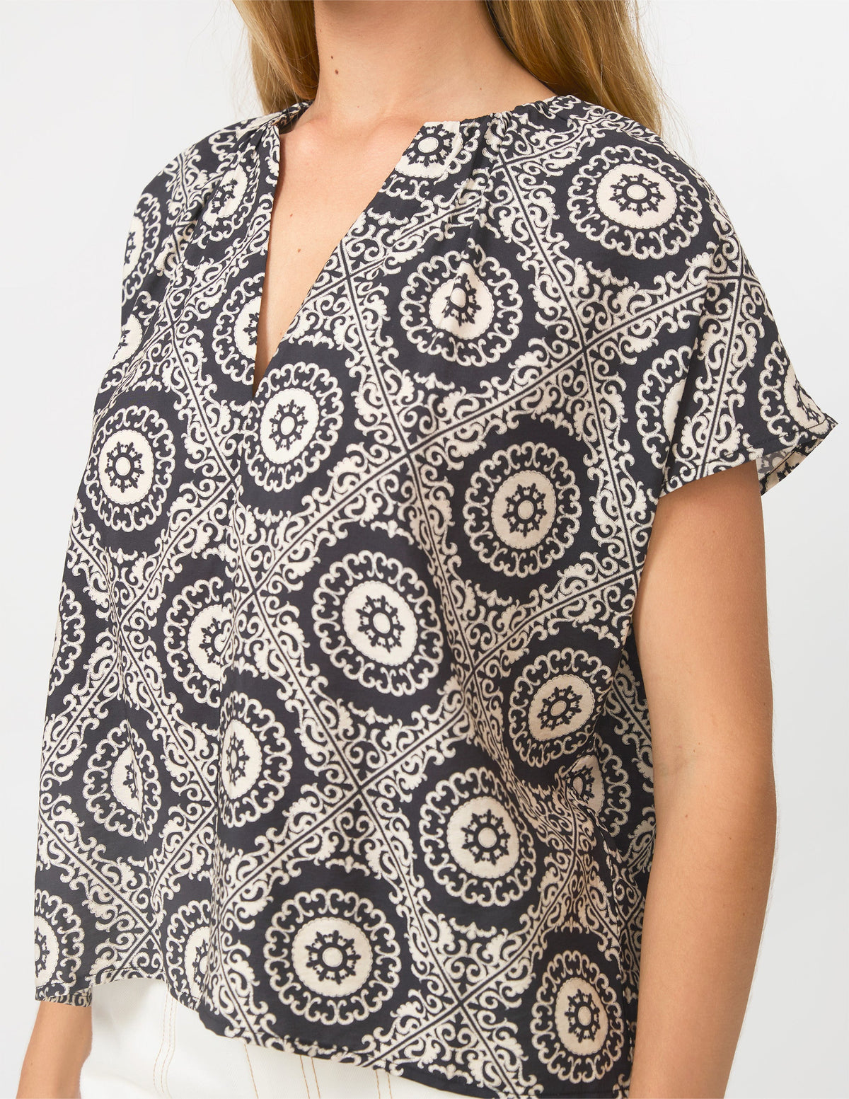 A woman wearing a short-sleeve blouse with a black and off-white bohemian mandala pattern, shown from the chest down against a plain white background.