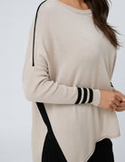 A woman wearing a cream-colored knit sweater with black contrast panels and black striped detailing on the cuffs, shown against a plain light gray background.