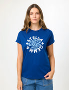 A women wearing a blue short sleeve t-shirt in front of a nuetral background