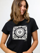 A woman wearing a black short-sleeve t-shirt with a large white square mandala graphic on the chest, set against a plain light gray background.