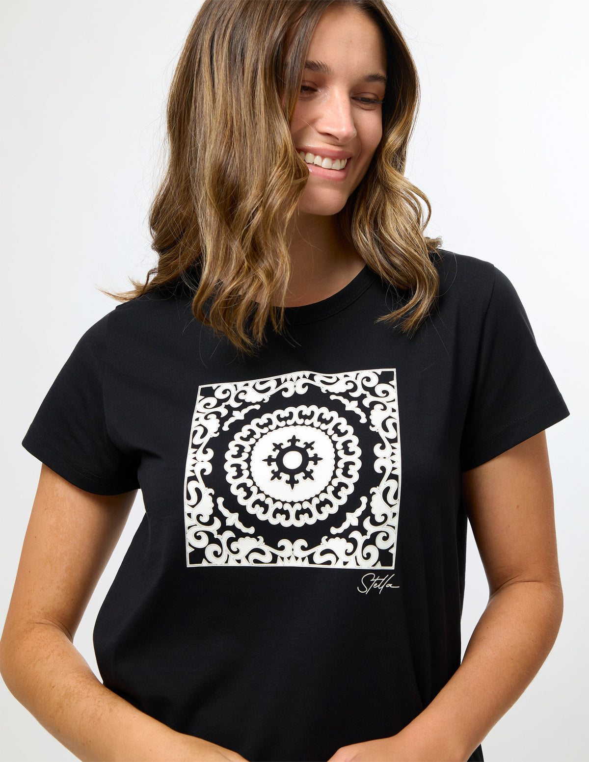 A woman wearing a black short-sleeve t-shirt with a large white square mandala graphic on the chest, set against a plain light gray background.